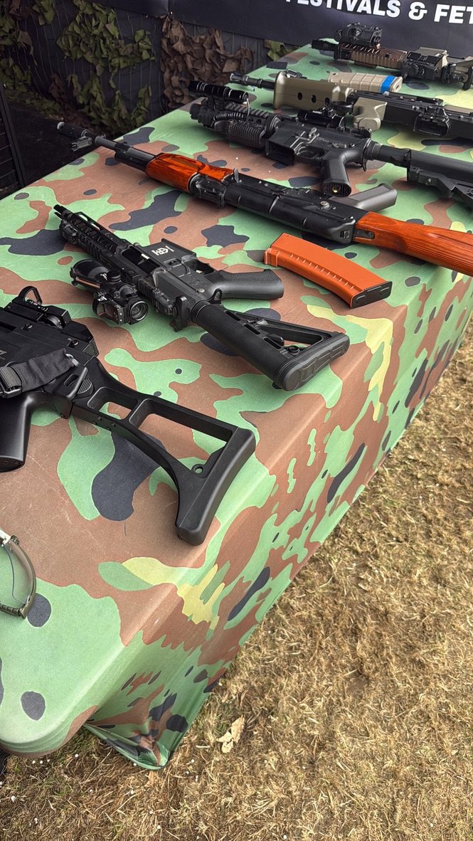 Replica rifles and pistols laid out on the camouflage-covered range table
